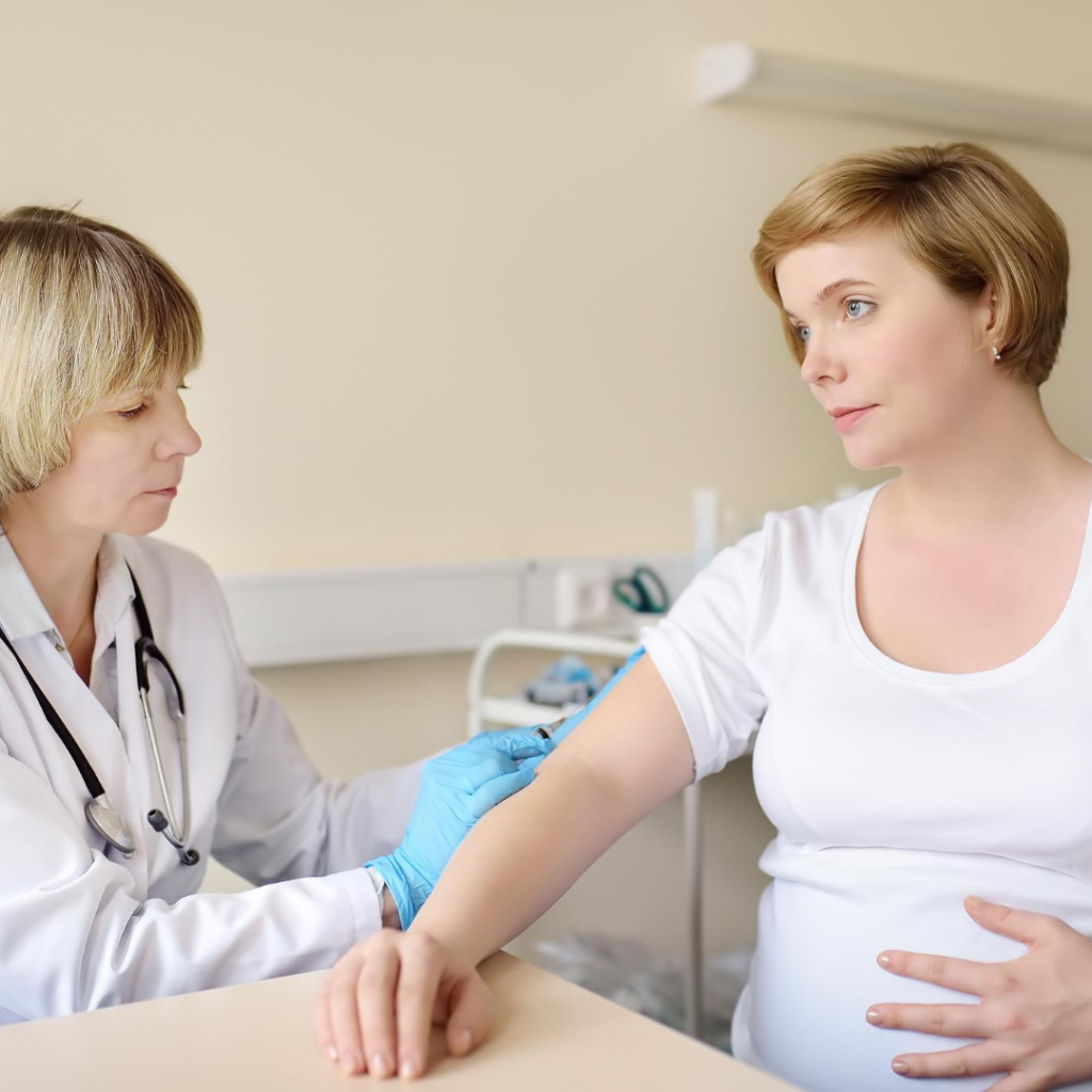 A female gynecologist near Queens, wearing gloves, administers an injection to a pregnant woman’s arm in a medical office. The woman sits, holding her belly, and looks thoughtfully at the professional.