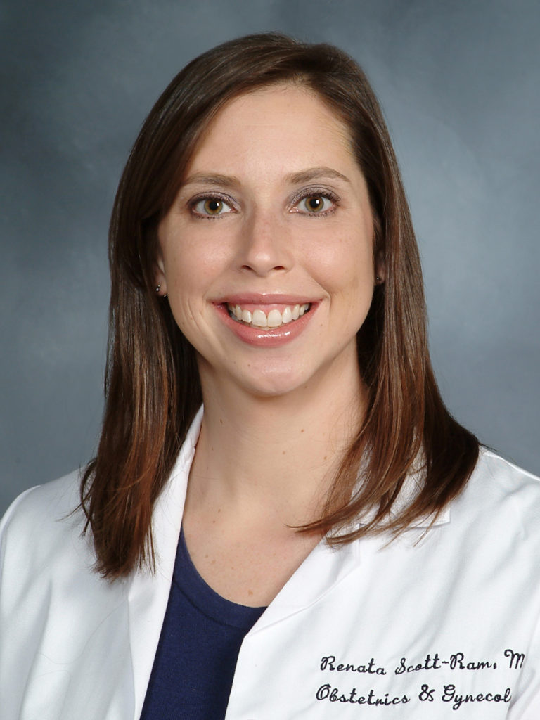 A woman with straight brown hair, wearing a white medical coat over a navy top, smiles at the camera against a gray background. The coat has embroidered text reading “Renata Scott-Ram, M Obstetrics & Gynecol.”.